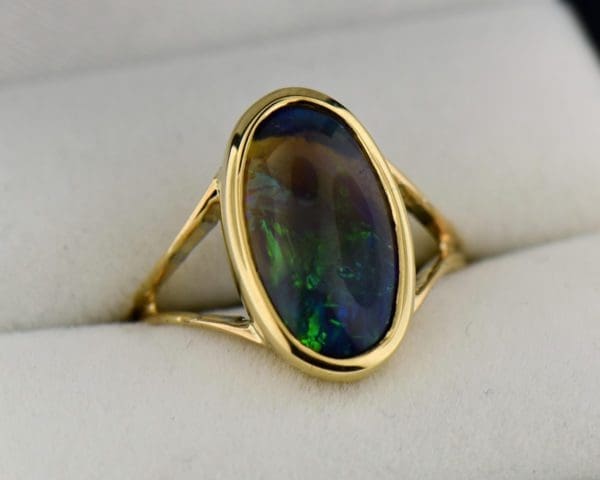 oval black crystal opal solitaire ring in yellow gold bezel with split shank